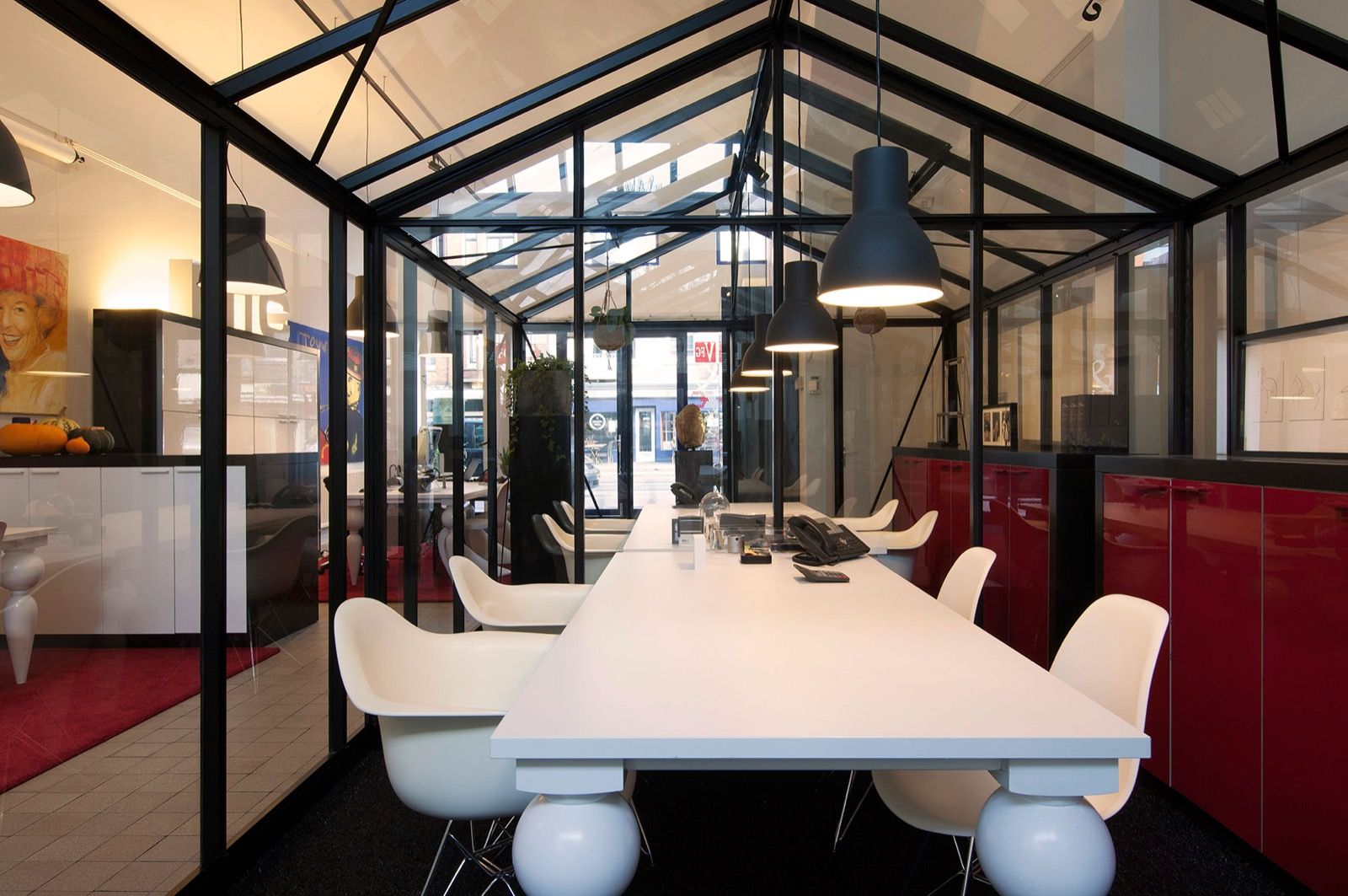 Spreekkamer van glas met witte tafel, witte stoelen en rode kasten