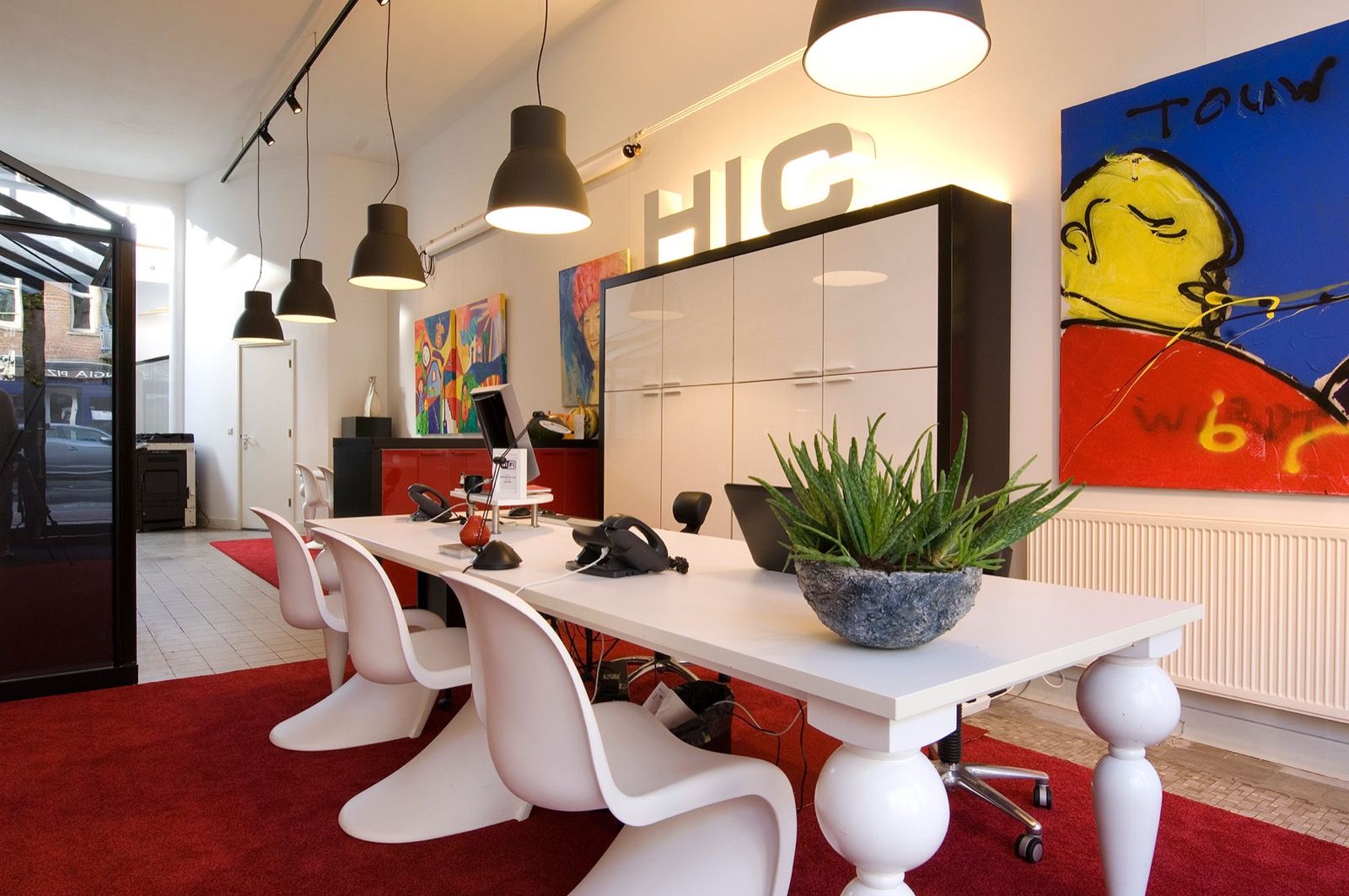 Het kantoor van Hypotheek Informatie Centrum: lange witte tafels op rood tapijt, met de letters HIC aan de wand